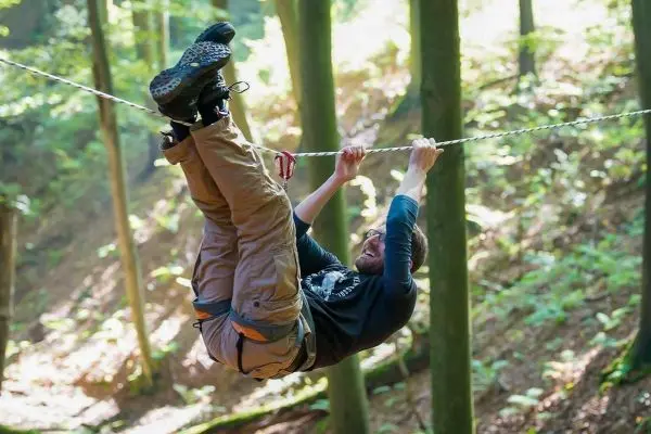 Person hängt kopfüber an einer Seilbrücke zwischen Bäumen