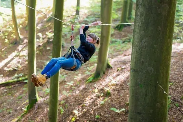 Person schwingt an einer Seilbrücke zwischen Bäumen