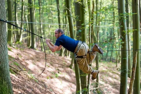 Person schwingt an einer Seilbrücke zwischen Bäumen