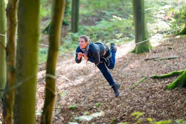 Person schwingt an einer Seilbrücke zwischen Bäumen im Wald