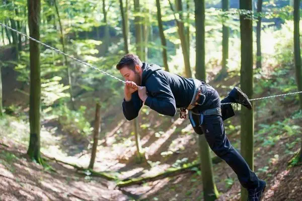 Person schwingt an einer Seilbrücke zwischen Bäumen im Wald