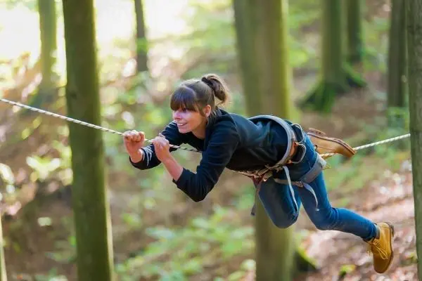Person schwingt an einer Seilbrücke zwischen Bäumen im Wald