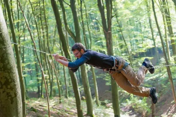 Person schwingt an einer Seilbrücke zwischen Bäumen im Wald