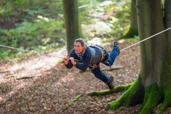 Person schwingt an einer Seilbrücke zwischen Bäumen im Wald