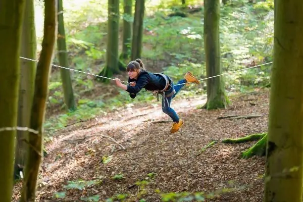 Person schwingt an einer selbstgebauten Seilbrücke zwischen Bäumen