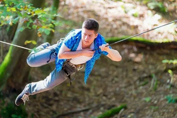 Person schwingt an Seil über den Boden im Wald