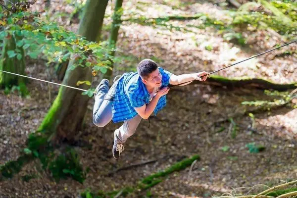Person schwingt an Seil zwischen Bäumen
