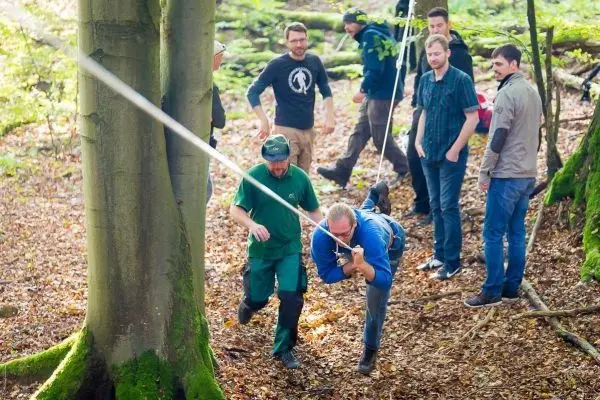 Person schwingt an Seil zwischen Bäumen, andere beobachten