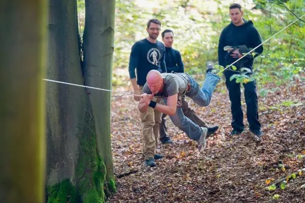 Person schwingt an Seil zwischen Bäumen, andere Personen beobachten
