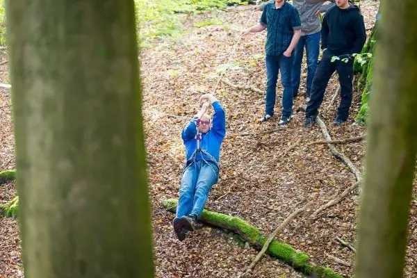 Person schwingt an Seil zwischen Bäumen, andere Personen beobachten