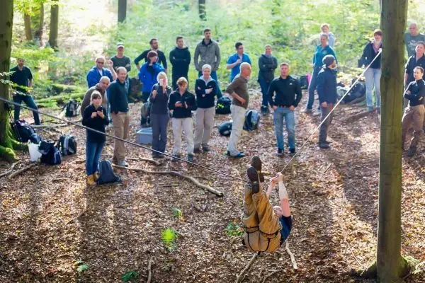 Person schwingt an Seil zwischen Bäumen, Gruppe schaut zu beim Überlebenstraining