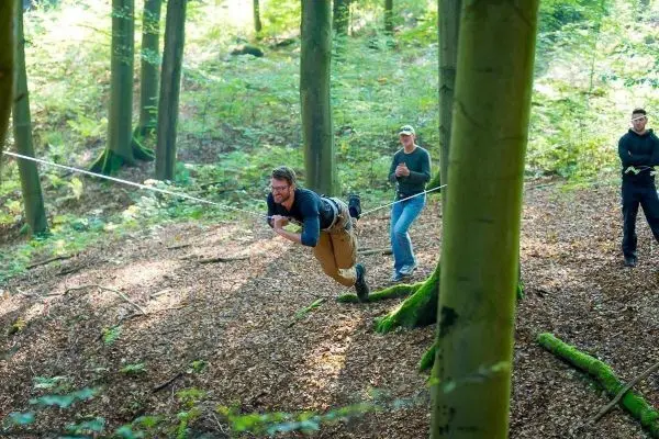 Person schwingt an Seil zwischen Bäumen im Wald