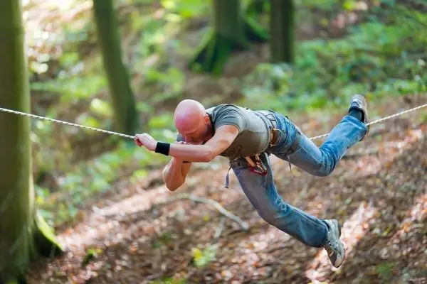 Person schwingt an selbstgebauter Seilbrücke durch den Wald