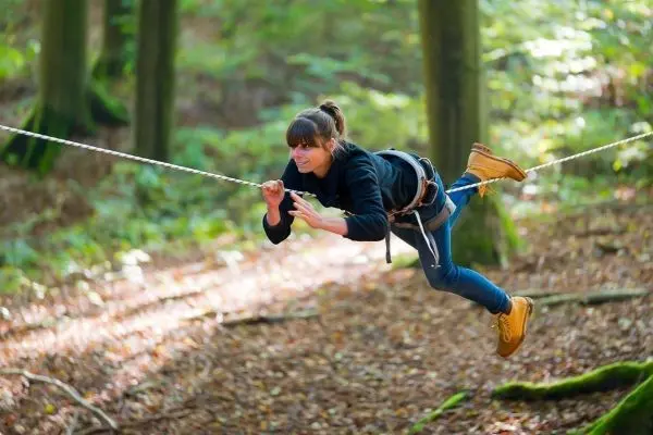 Person schwingt an selbstgebauter Seilbrücke durch den Wald beim Survival Training