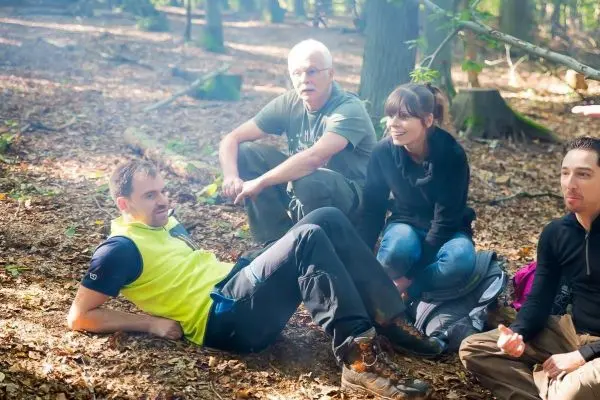 Person sitzt auf dem Boden, umgeben von drei weiteren Personen im Wald