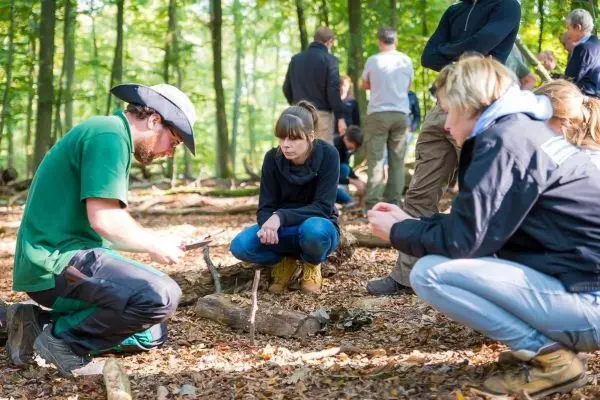 Person zeigt einer Gruppe das Bearbeiten von Holz im Wald