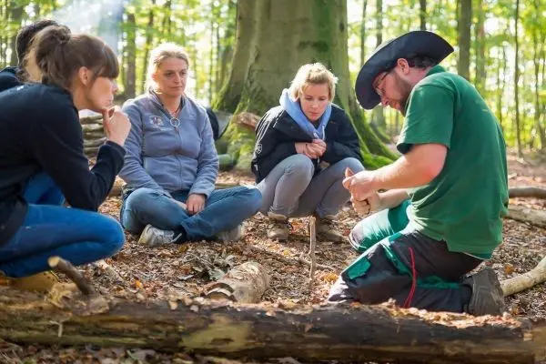Person zeigt Gruppe das Schnitzen im Wald beim Survival Training