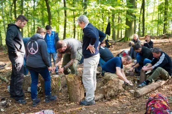 Teilnehmende bearbeiten Holzstücke auf Baumstümpfen im Wald