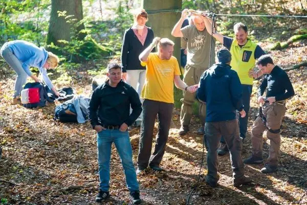 Teilnehmer sichern sich mit Gurten für eine Seilbrückenübung im Wald