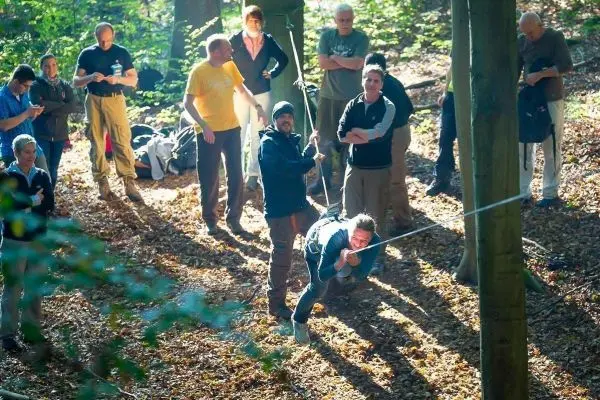 Teilnehmer üben das Abseilen an einer selbstgebauten Seilbrücke zwischen Bäumen