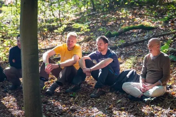 Vier Personen sitzen im Wald auf dem Boden und unterhalten sich