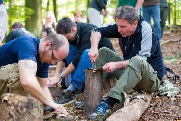 Zwei Personen bearbeiten Holzstücke mit Messern im Wald