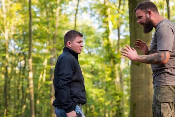 Zwei Personen diskutieren in einem Waldgebiet, umgeben von Bäumen