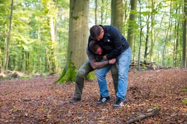 Zwei Personen üben eine Grifftechnik im Wald auf Laubboden