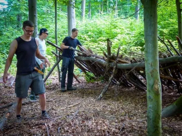 Drei Personen bauen eine Holzkonstruktion aus Ästen im Wald