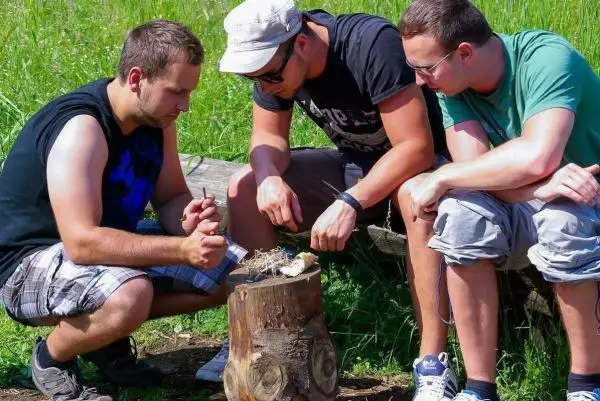Drei Personen bearbeiten Zunder auf einem Baumstumpf im Freien