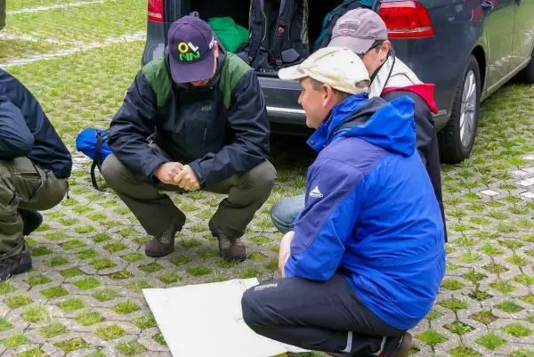 Drei Personen knien um eine Karte auf dem Boden, während ein Auto im Hintergrund steht