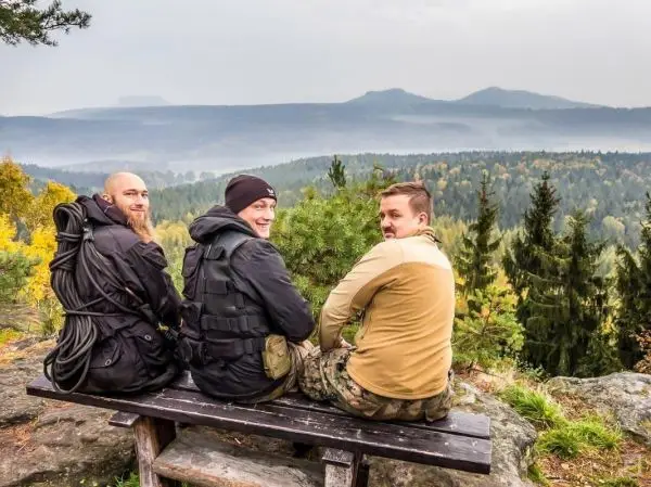 Drei Personen sitzen auf einer Bank und blicken auf eine bewaldete Landschaft
