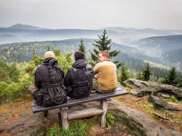 Drei Personen sitzen auf einer Bank und blicken auf eine bewaldete Landschaft