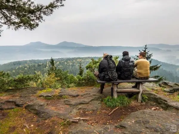 Drei Personen sitzen auf einer Bank und blicken auf eine bewaldete Landschaft