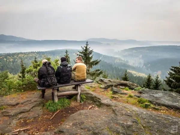 Drei Personen sitzen auf einer Bank und blicken auf eine bewaldete Landschaft