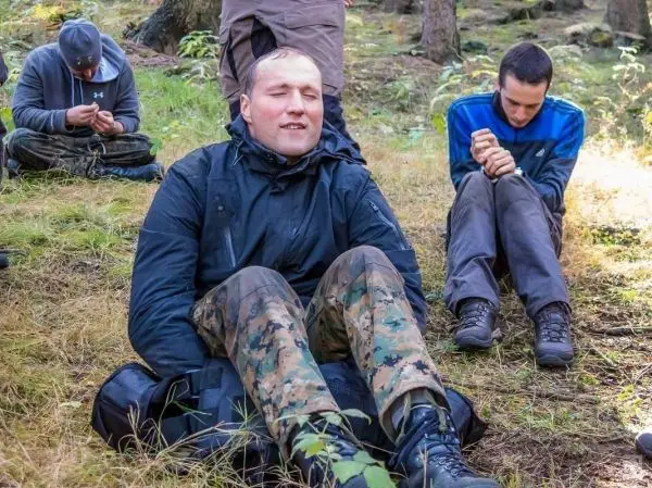 Drei Personen sitzen im Wald auf dem Boden und beschäftigen sich mit Ausrüstung