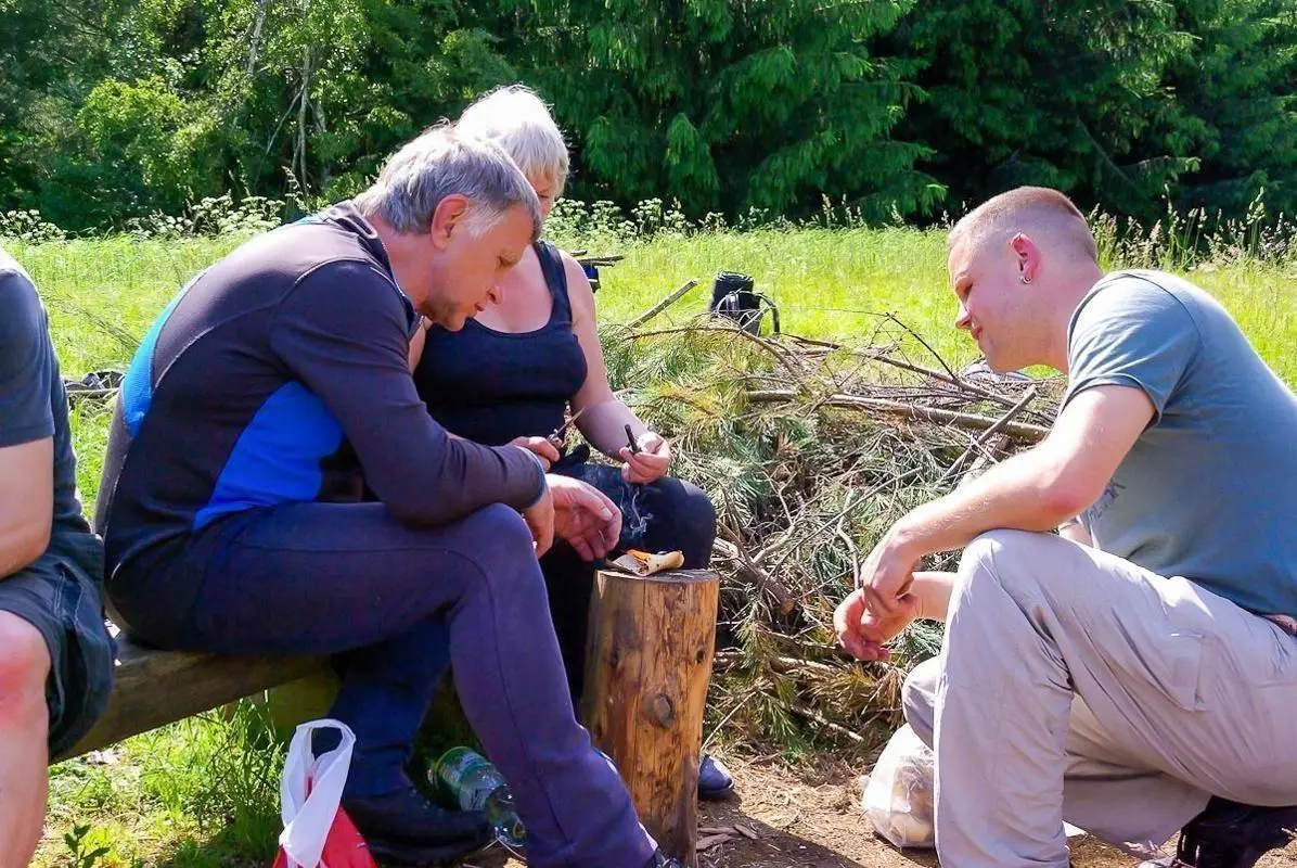 Drei Personen sitzen um einen Holzblock und bearbeiten mit einem Messer Holz