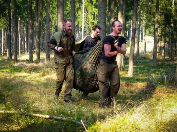 Drei Personen tragen eine improvisierte Trage durch den Wald