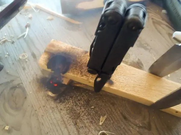 Feuerstahl erzeugt Funken auf einem Holzstück mit Glutnest