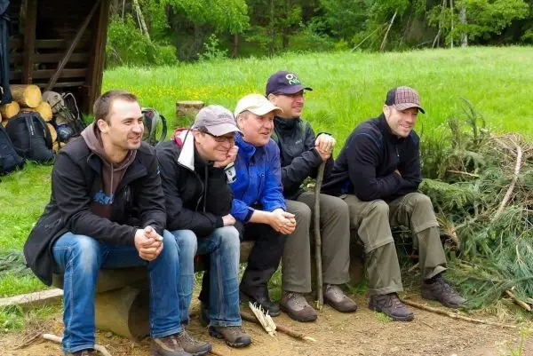Fünf Personen sitzen auf einem Holzstamm und unterhalten sich