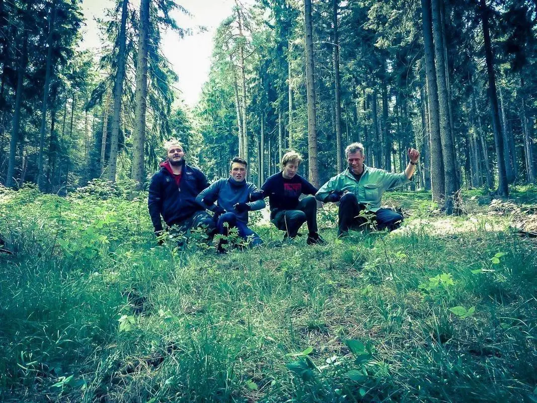 Gruppe sitzt im Wald auf dem Boden zwischen Bäumen und hohem Gras