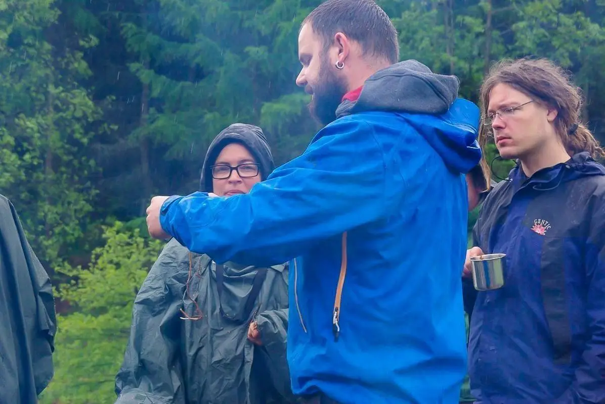 Gruppendiskussion über Outdoor-Techniken im Wald, Teilnehmer tragen Regenbekleidung