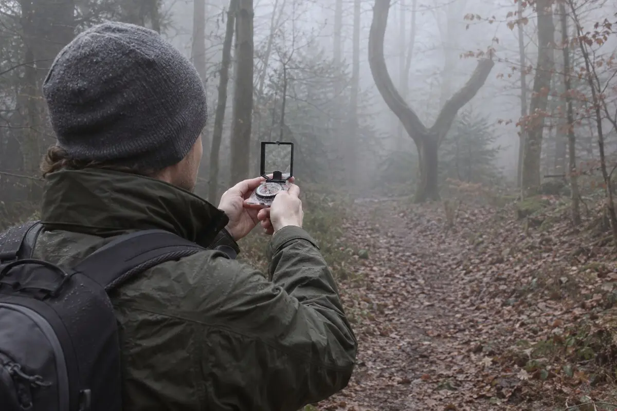 Navigator peilt mit einem aufgeklappten Spiegelkompass im Nebel einen markanten gegabelten Baum in kurzer Entfernung an