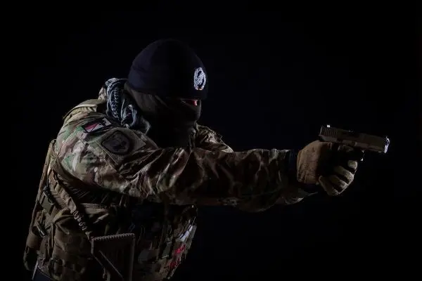 Mann in Tarnkleidung zielt mit einer Handfeuerwaffe nach vorne