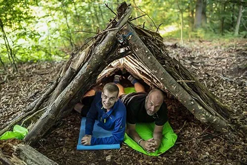 Zwei Teilnehmer in einer Notunterkunft aus Ästen im Wald