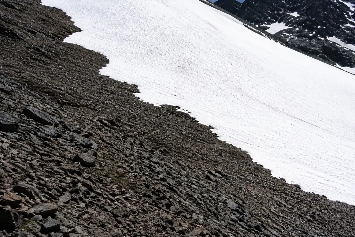 Helle Schneefläche neben dunklem Fels in der Sonne