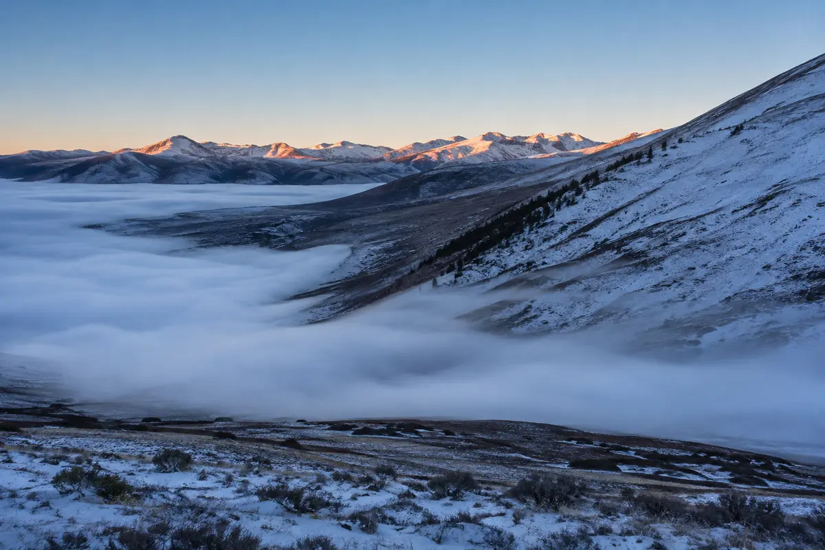 Kalter Nebel strömt einen Berghang ins Tal hinab