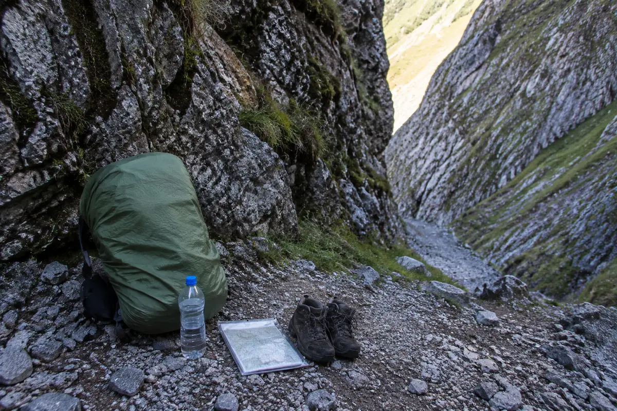 Rucksack, Wasser und Karte an einem geschützten Platz vor einem Felsdurchlass