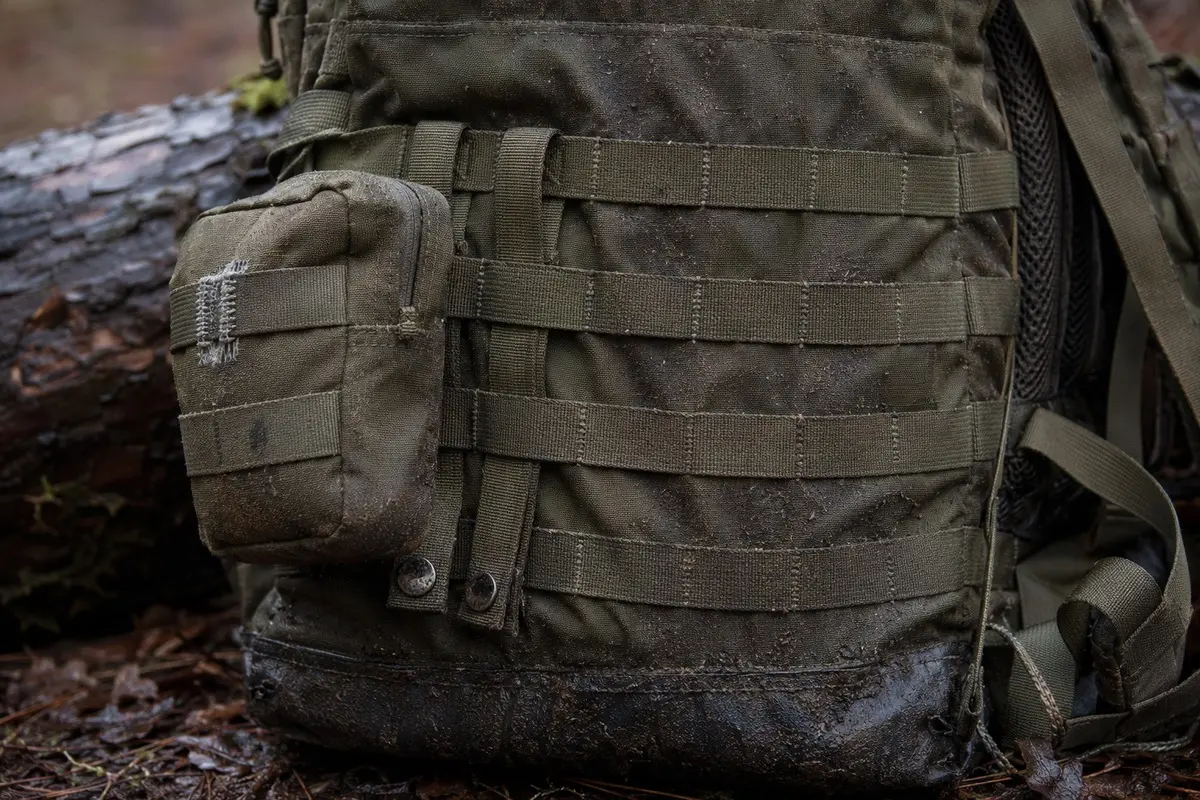 Verschmutzte MOLLE-Tasche mit eingefädelten Befestigungsriemen an einem gebrauchten Rucksack