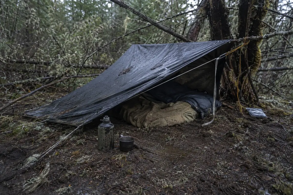 Hastig errichtetes regennasses Tarp-Biwak mit Schlafsack, Decke und Wasserbehälter